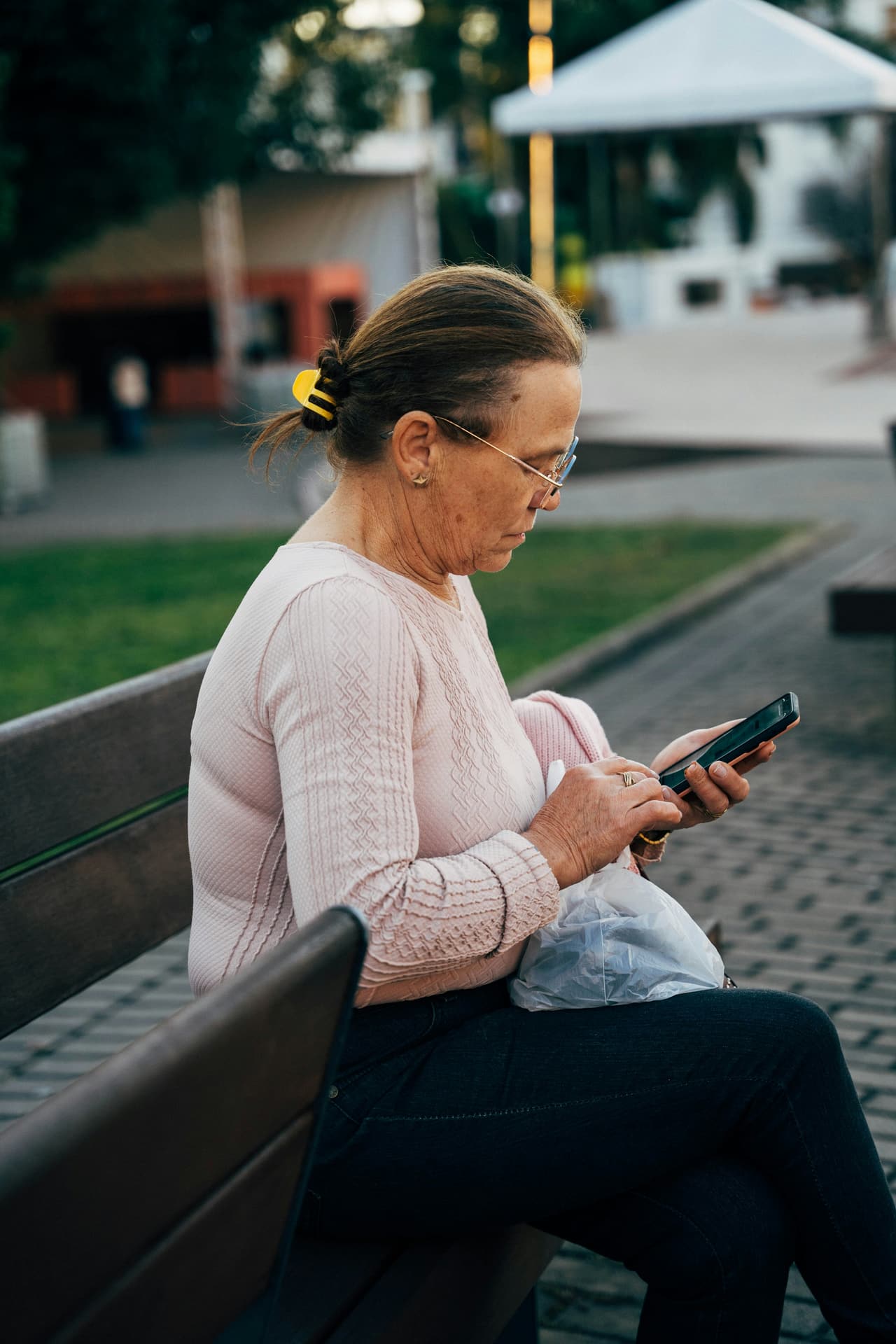 An older woman reading a message on her phone while sitting on a bench
