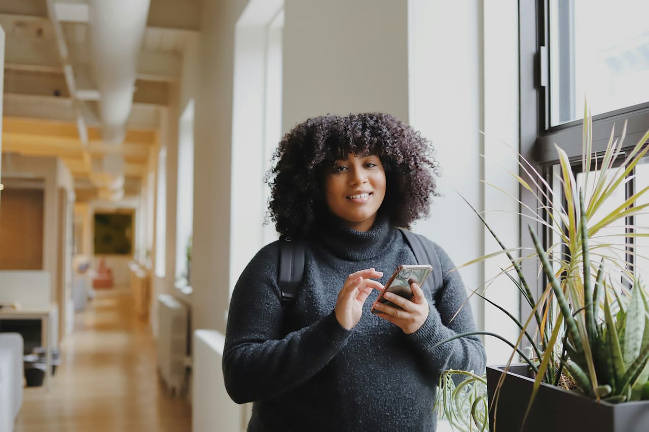 A Black woman by a window using her phone